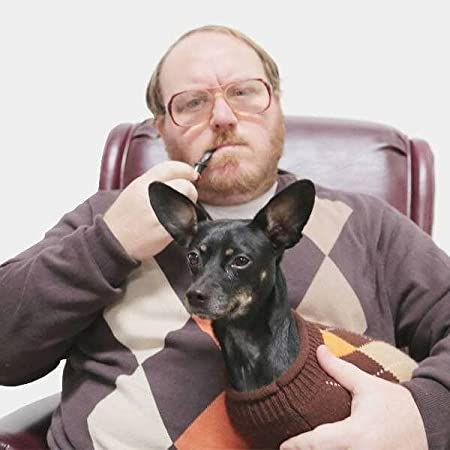 A man in glasses holds a dog in his lap and a pipe in his mouth.