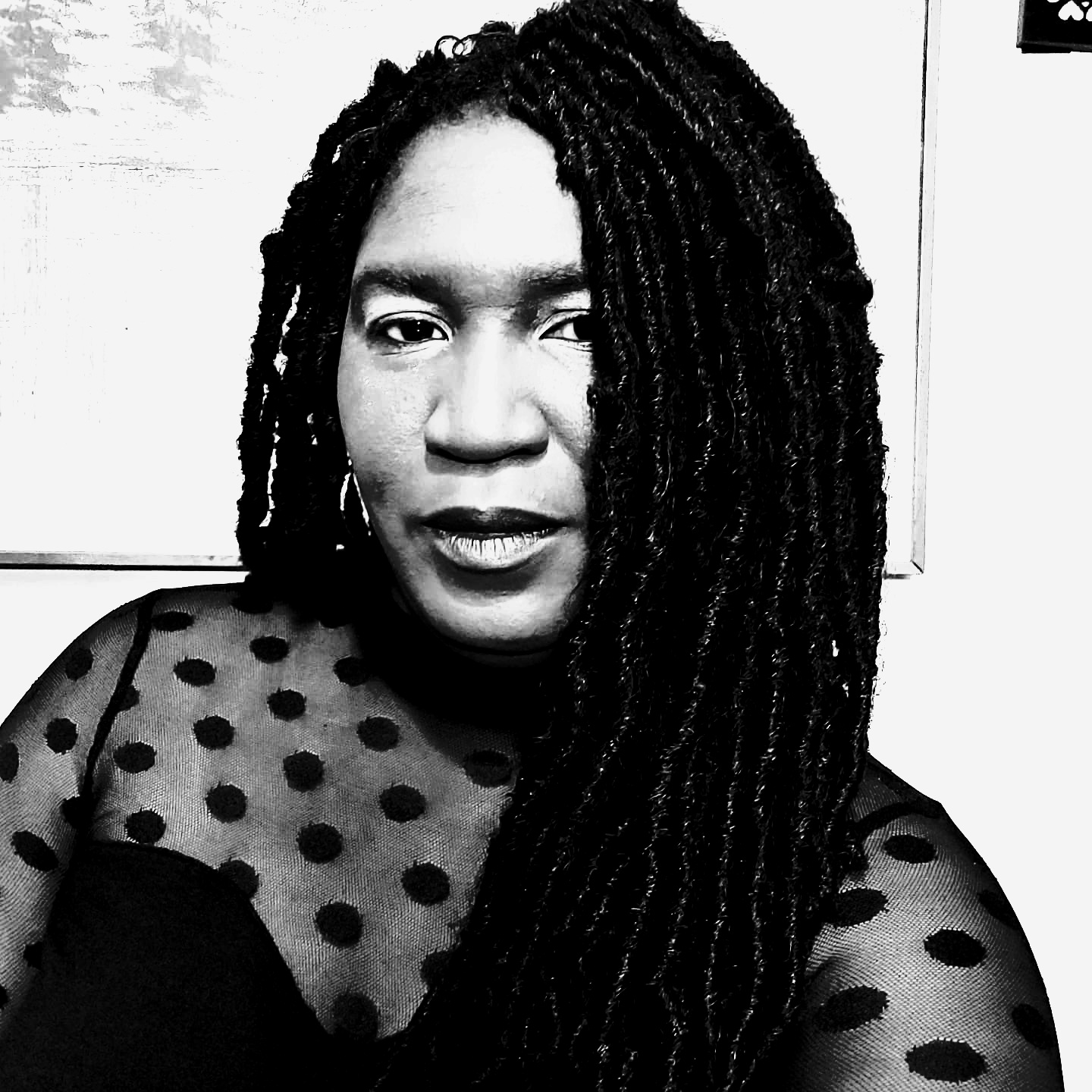 A black and white photo of a black woman with long braided hair from the chest up, looking at the camera.
